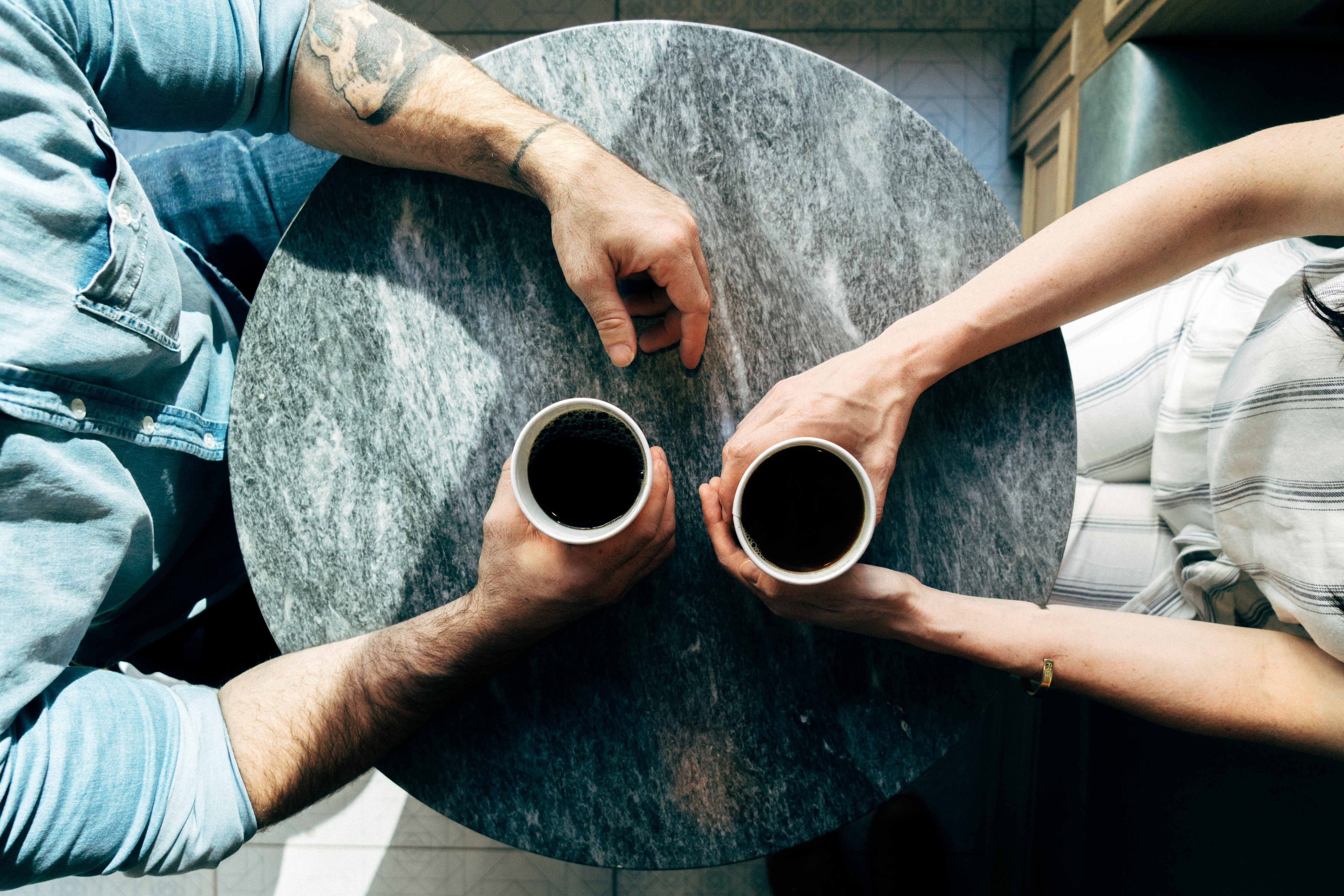 Overhead shot of a man and woman sitting at a round marble table drinking coffee.