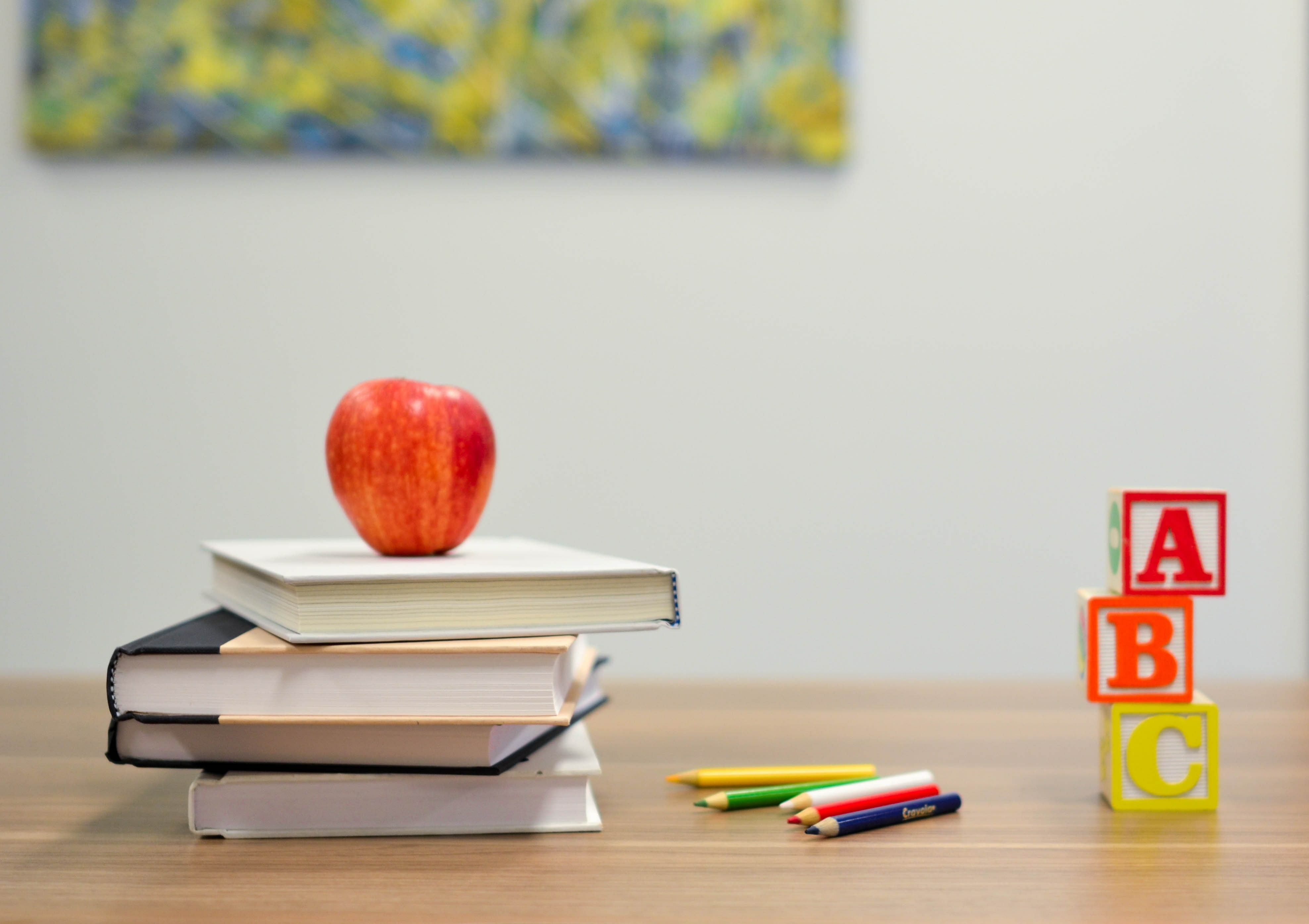 A red apple sitting on top of three books with colorful wooden alphabet blocks on the right.