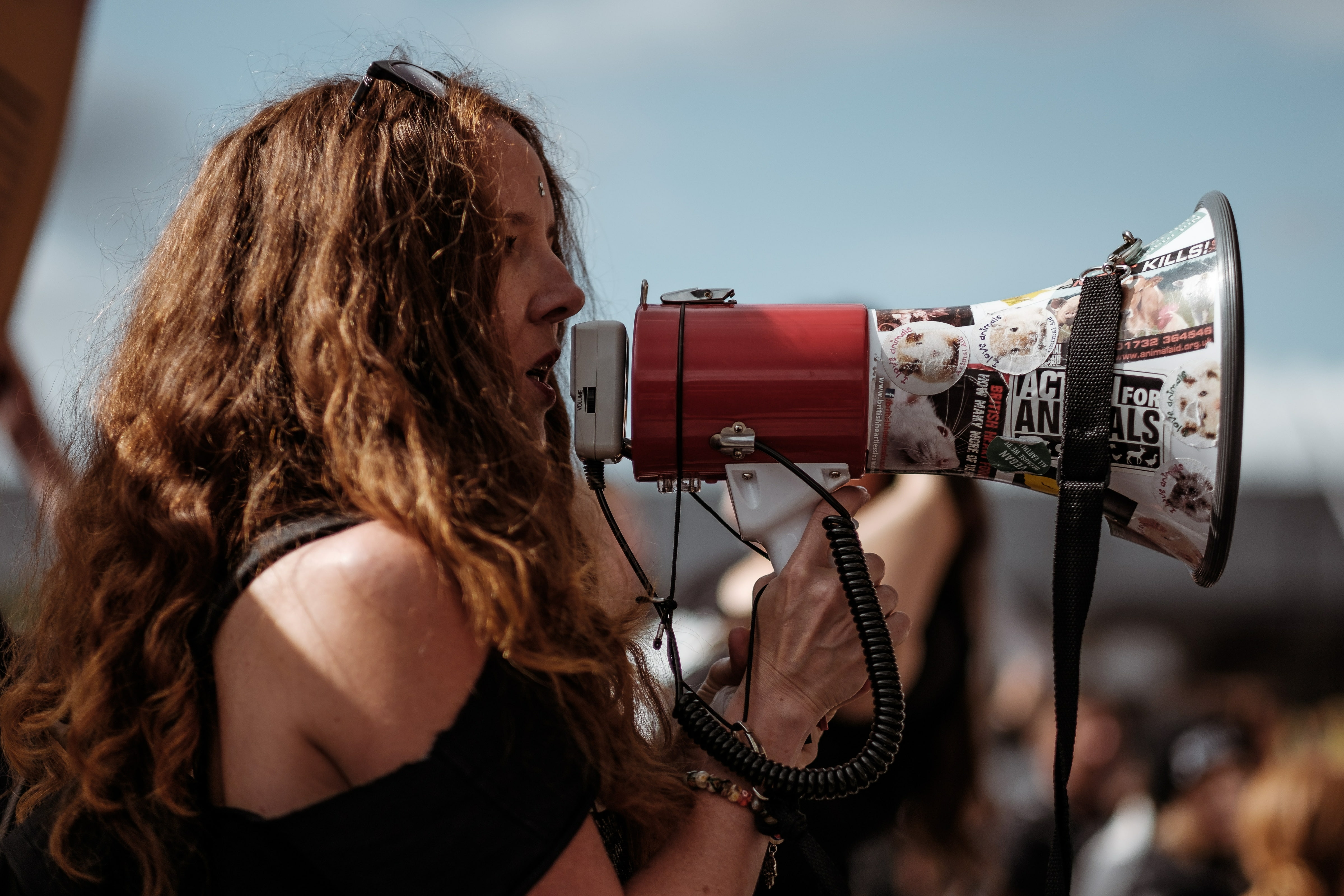 Activist with curly brown hair holding a megaphone covered in stickers.