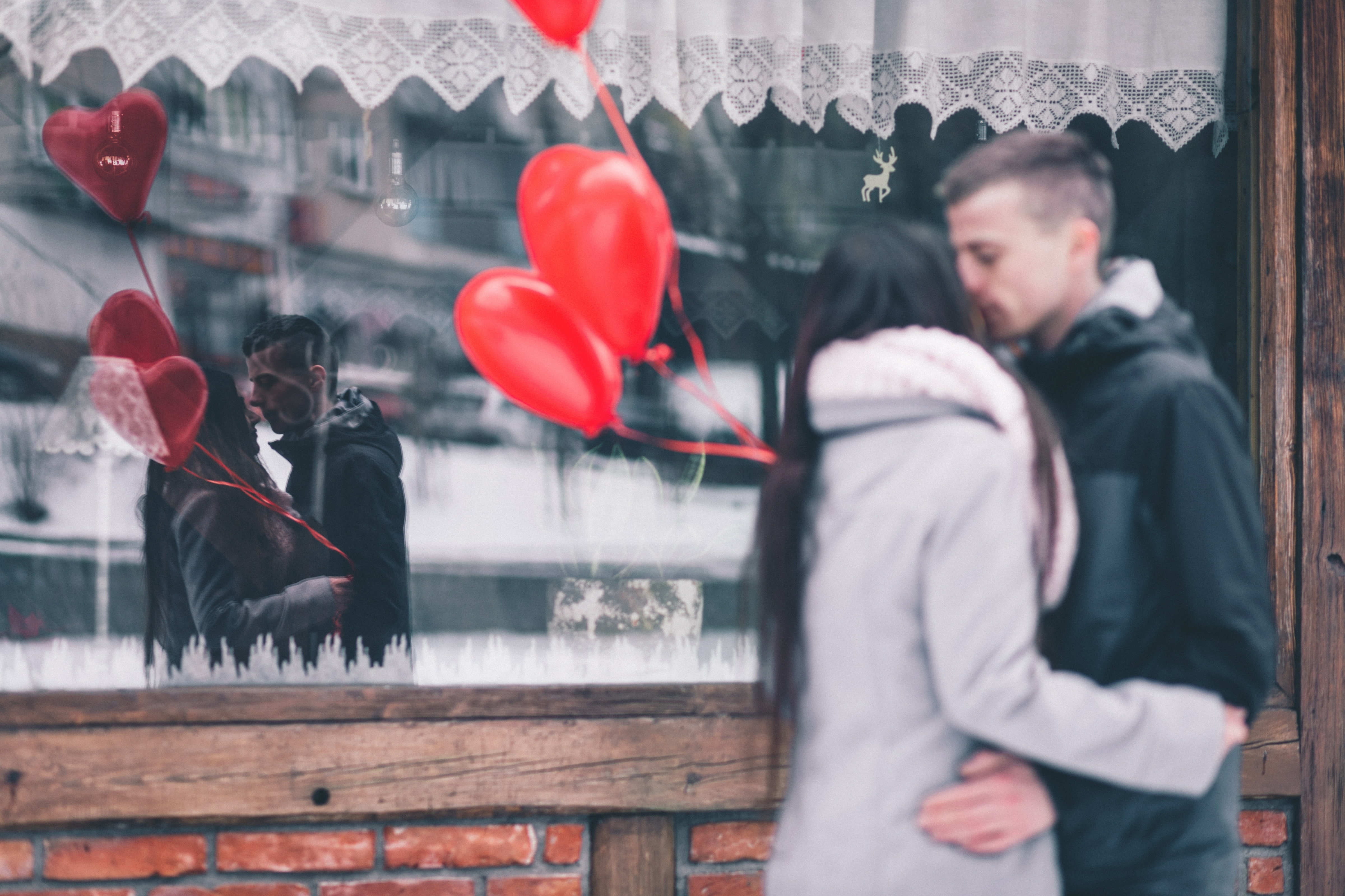 A couple kissing in front of a store window that also catches their reflection.