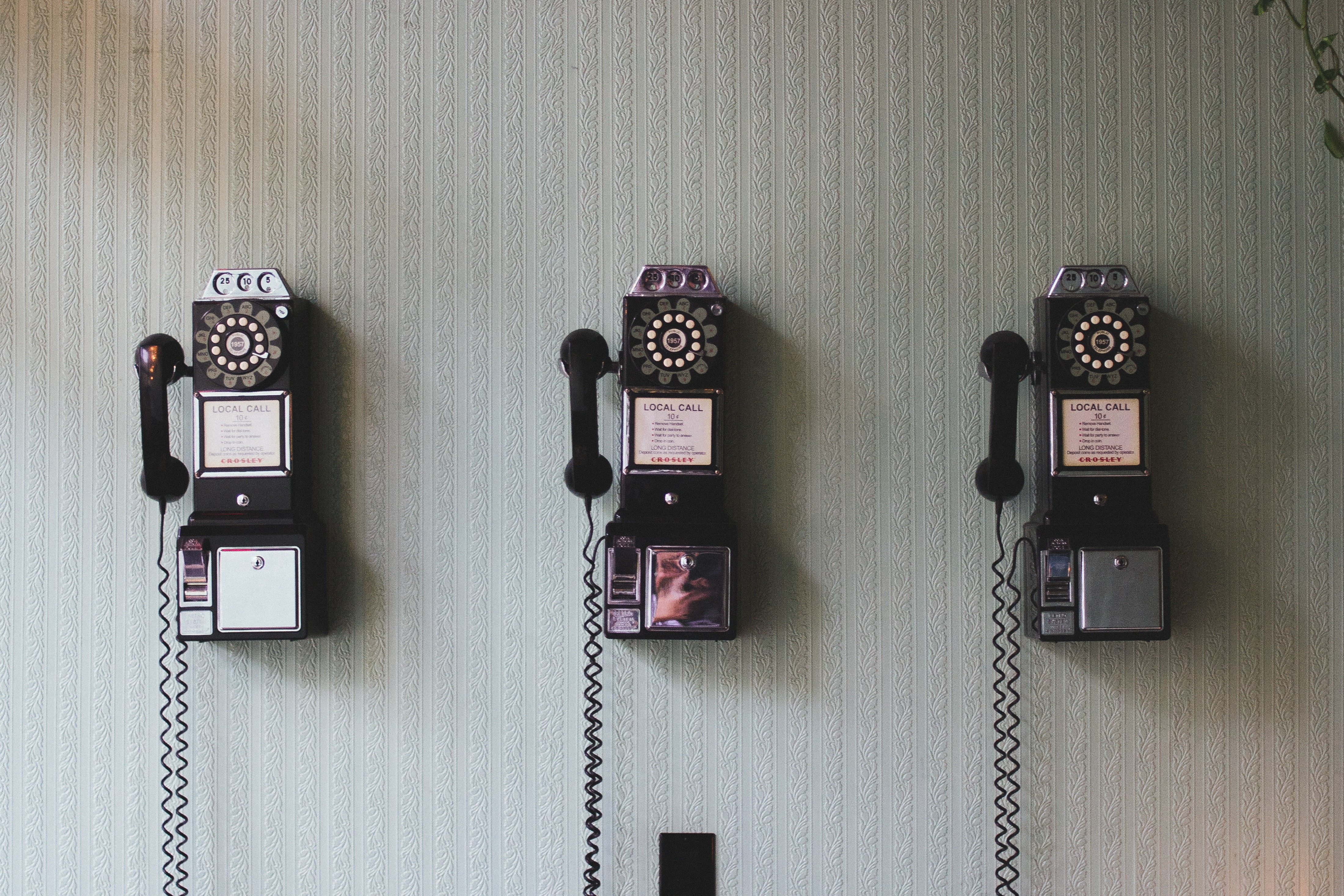Three rotary phones on a wall.