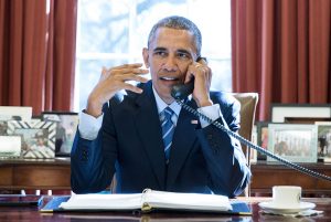 Barack Obama sitting at his desk on the phone.
