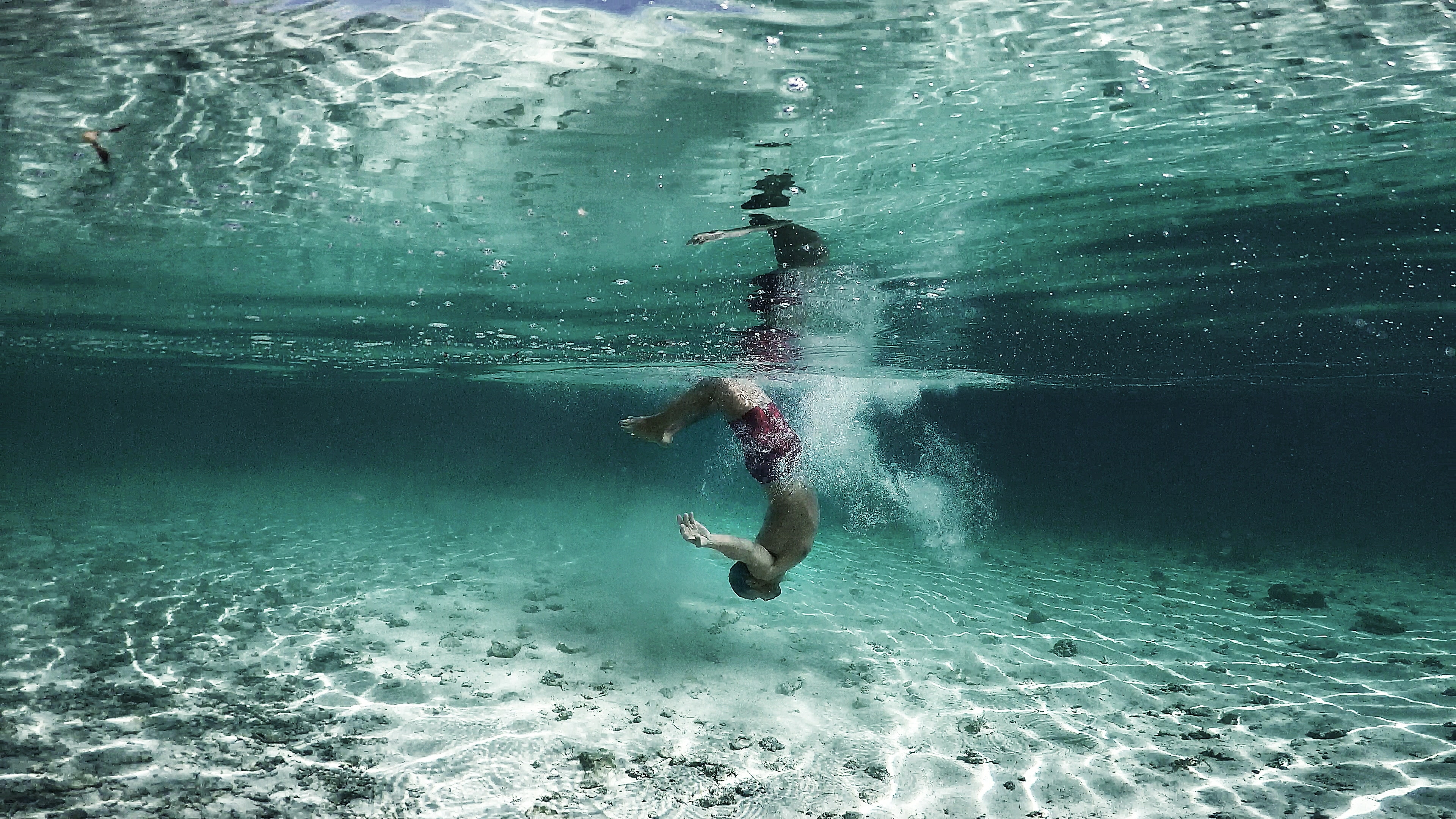 A man dives into shallow water that is crystal clear.