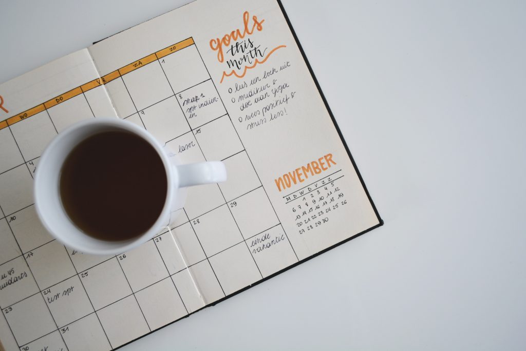 A cup of coffee next to a goal setting calendar on a desk.