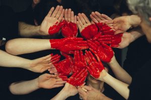 Many hands with red paint on the palms that make a heart shape.