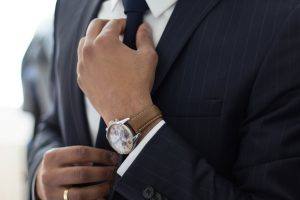 man wearing suit and watch adjusting his tie