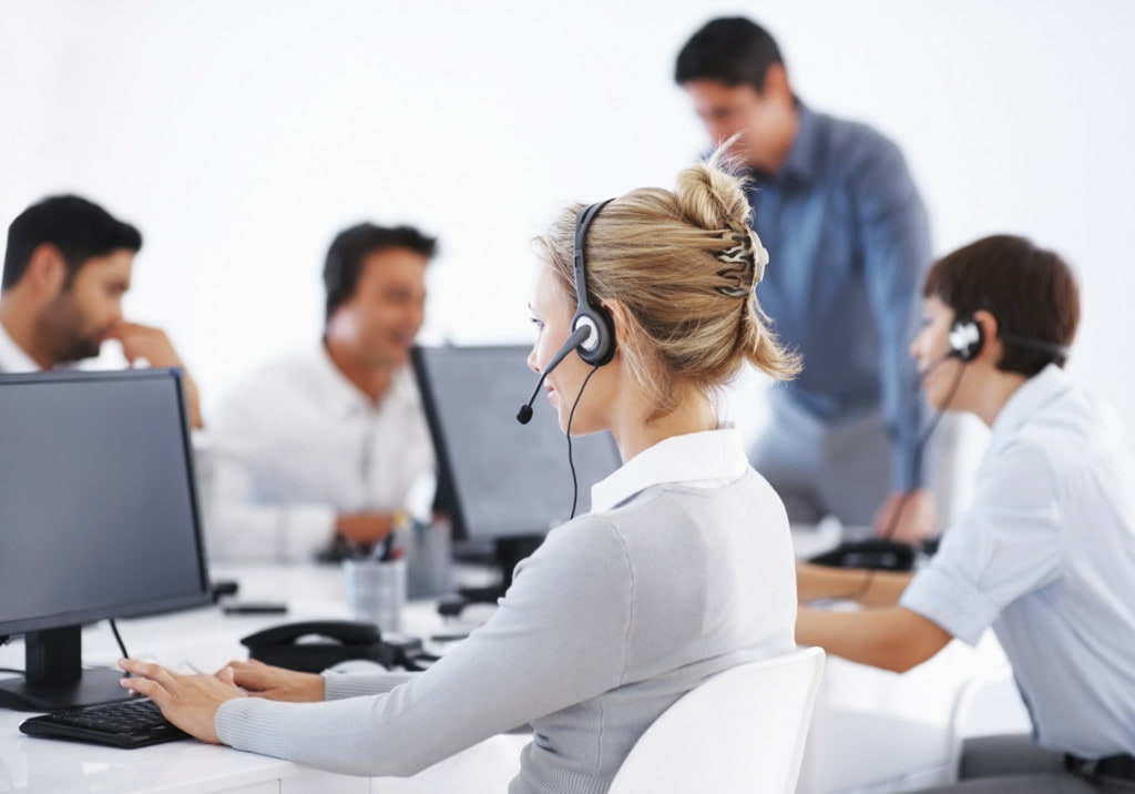 Business woman wearing headset working on computer with colleagues
