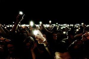 large crowd of people standing in the dark waving their cellphones with the flashlight feature enabled
