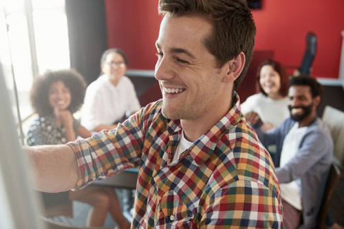 a man smiles while presenting to a small group of diverse men and women in a room