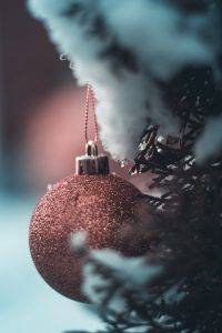 sparkly holiday ornament hanging from snowy pine tree branch