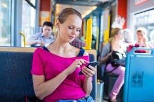 Women in pink shirt riding bus looking at mobile phone.
