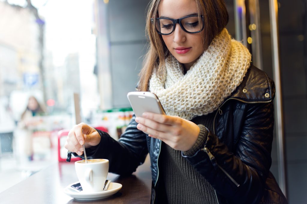 Women at coffee shop drinking coffee and looking at phone.