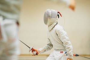 child in fencing uniform stands at the ready