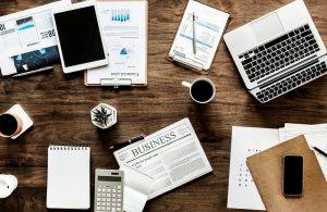 cluttered wooden desk with coffee mug and papers with electronics