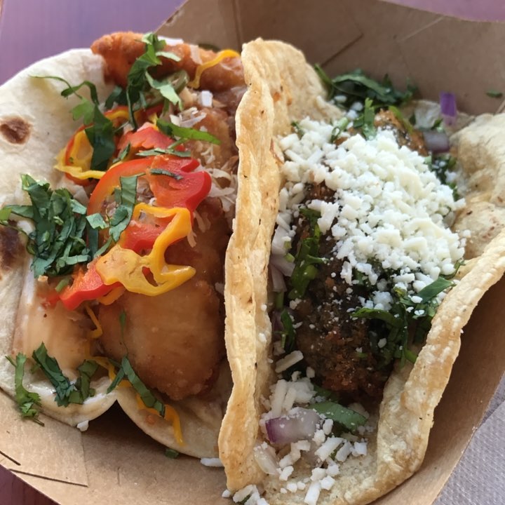 Two tacos with unique ingredients in a food truck serving dish.