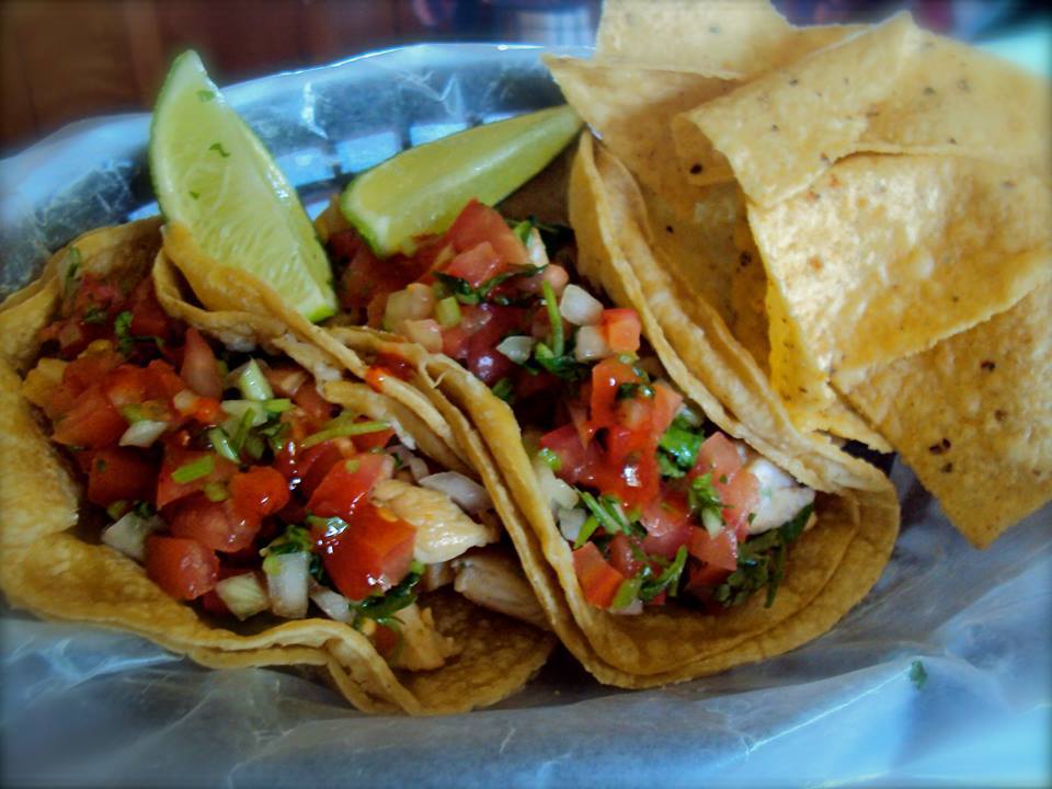 Two fresh tacos with salsa and a lime in a basket with tortilla chips.