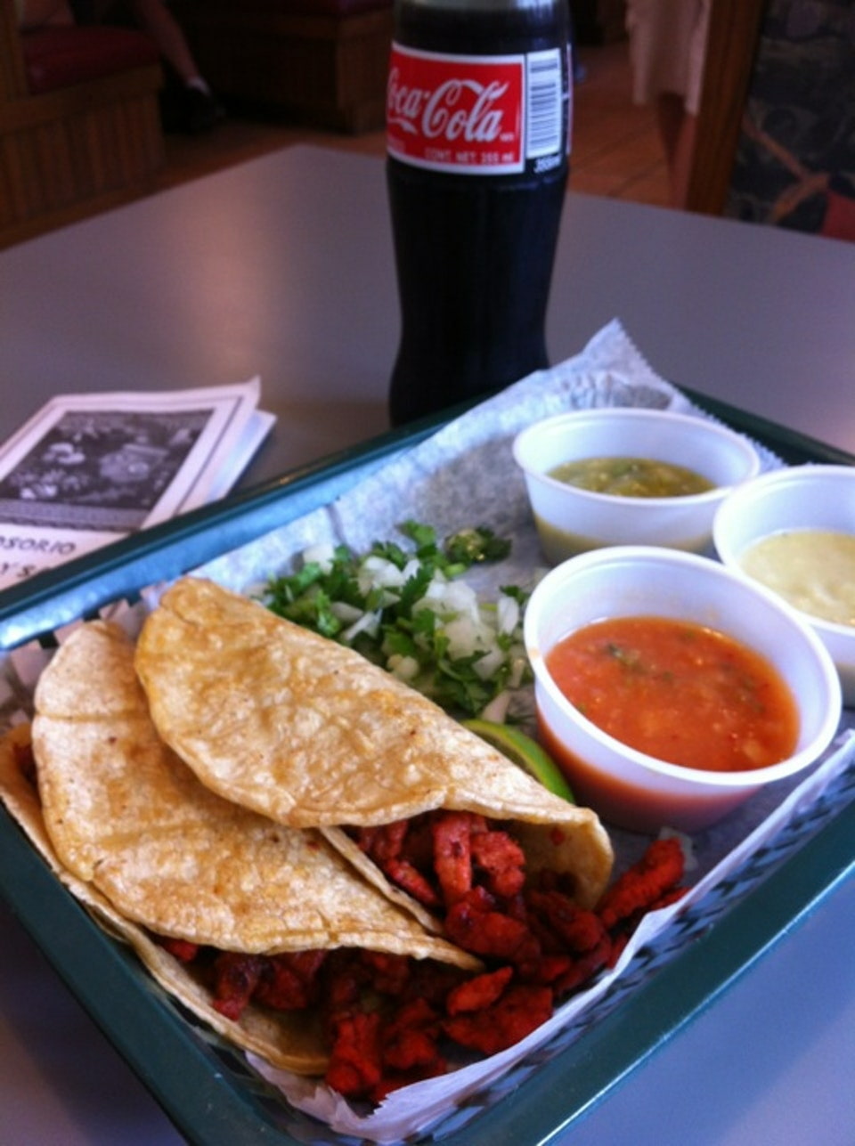 Two tacos on a platter with three sides of salsa and a coke in a glass bottle.