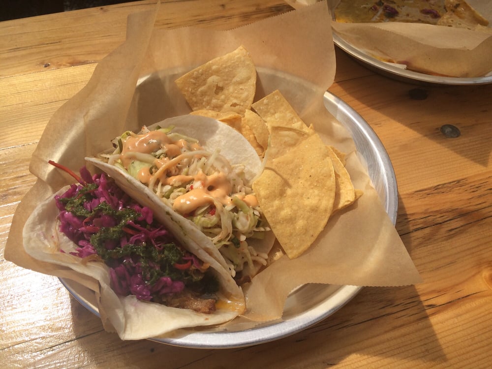 Two tacos on a pie tin plate with tortilla chips.