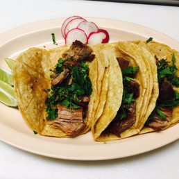 Three tacos on a white platter with thinly sliced radishes.
