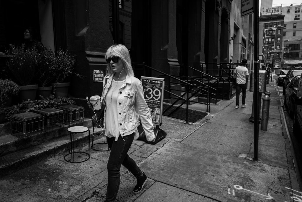 A black and white image of a women holding a coffee walking down a city street.