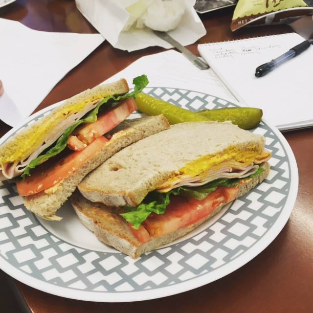 A deli sandwich with ham, lettuce, tomato and mustard on white bread.