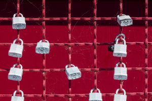 Several locks attached to a red metal fence.