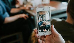 A person taking a video on their iPhone of a group of people eating at a restaurant.