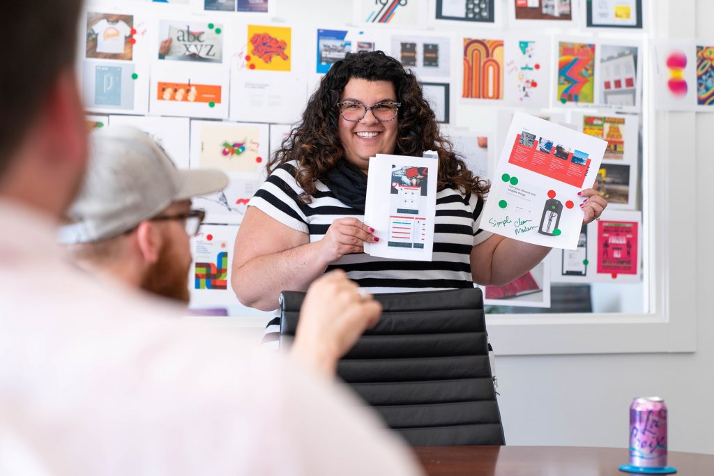 A woman holding two papers with graphics and wall behind her.