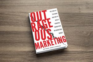 Scott Dikkers Outrageous Marketing book sitting on a table.