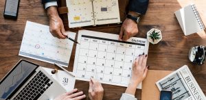 Hands from several people working and pointing to dates on a calendar.