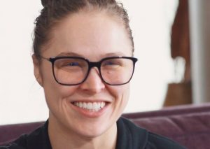 ronda rousey, a professional wwe wrestler smiles while wearing black framed glasses