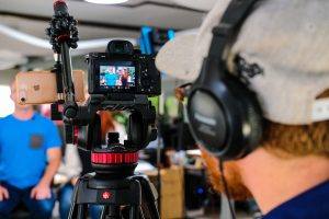 a man prepares to film a man and woman sitting on stools