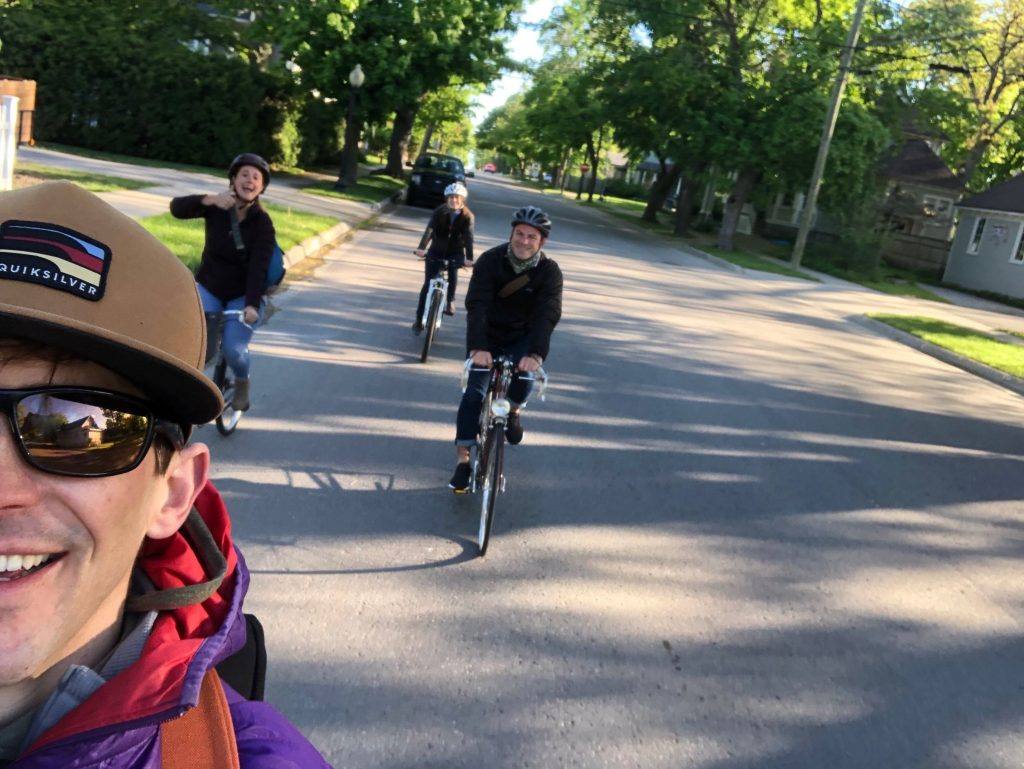 selfie taken by smiling man with three people biking behind him