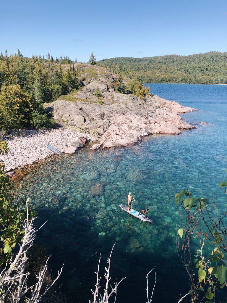 person standing on paddle board near shoreline of a lake