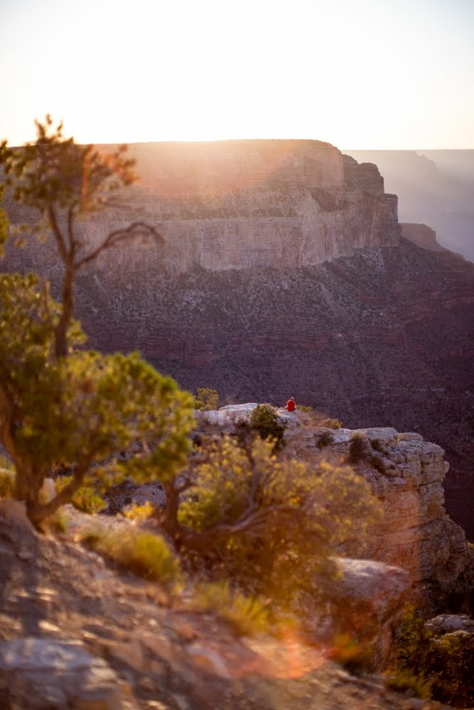 person sitting on faraway cliff with more cliffs in the distance