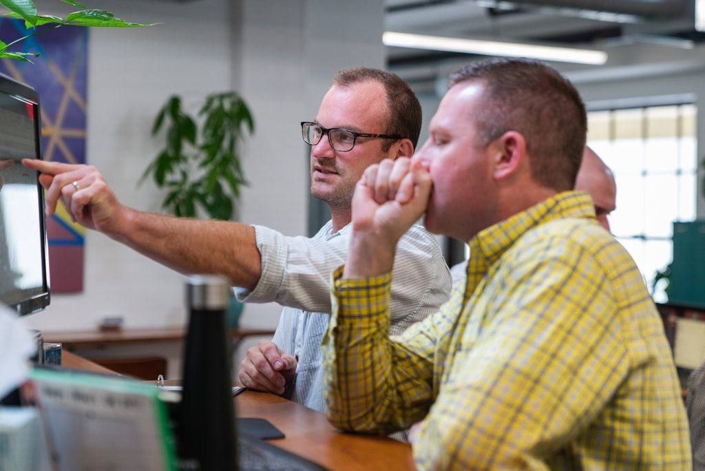 two men sitting at a computer and talking