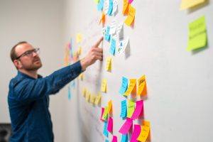 man pointing to colorful sticky notes stuck to a wall