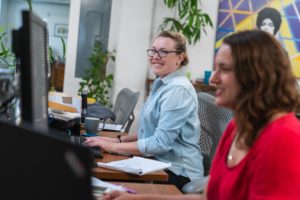 two women sitting at computers in an open office setting