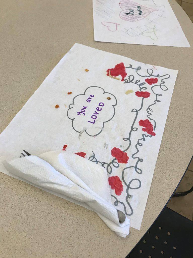 a placemat saying "you are loved" on a table where meals for homeless people are served