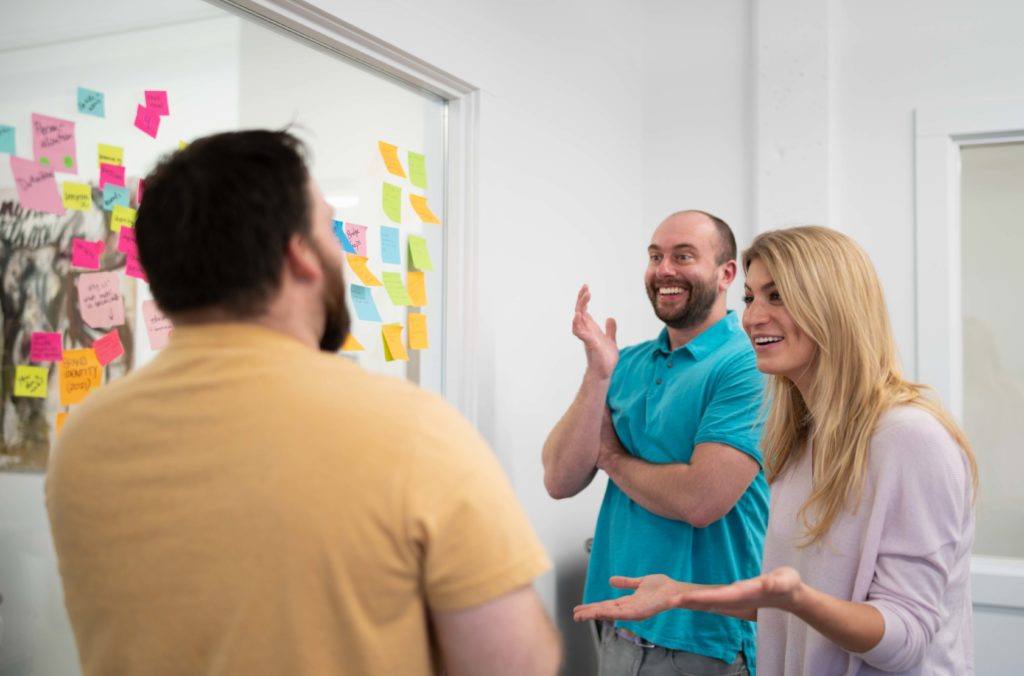 Three people having an exciting conversation while planning marketing strategies with sticky notes on the wall