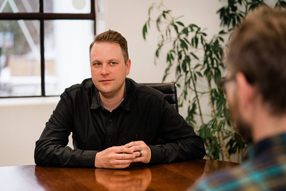 Man sits a table, being interviewed by another person