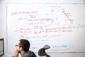 Website developer works on his computer while notes from a team brainstorm are still on the whiteboard behind him