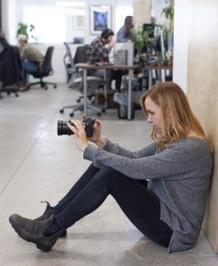 oneupweb videographer emily nelson composes a shot with her camera while sitting on the ground