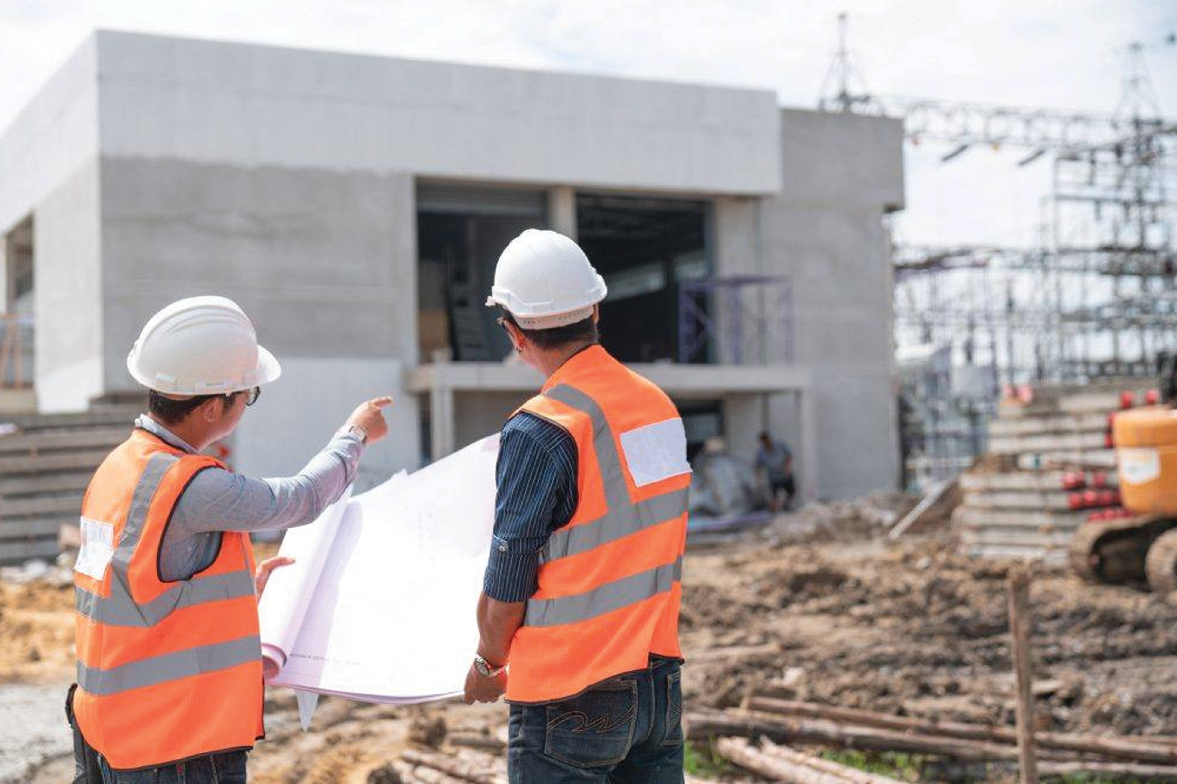 Two McCarthy construction engineers review a blueprint and point at an unfinished concrete building