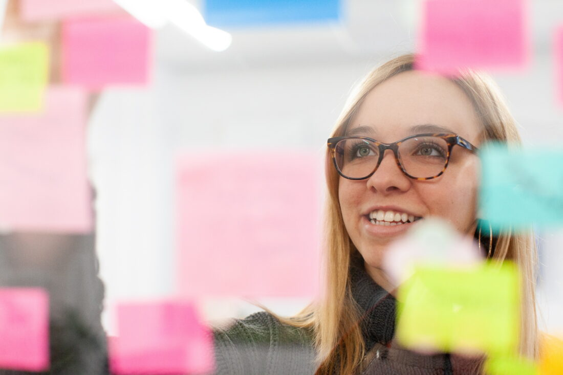 Woman reads sticky notes on a window to brainstorm marketing strategies