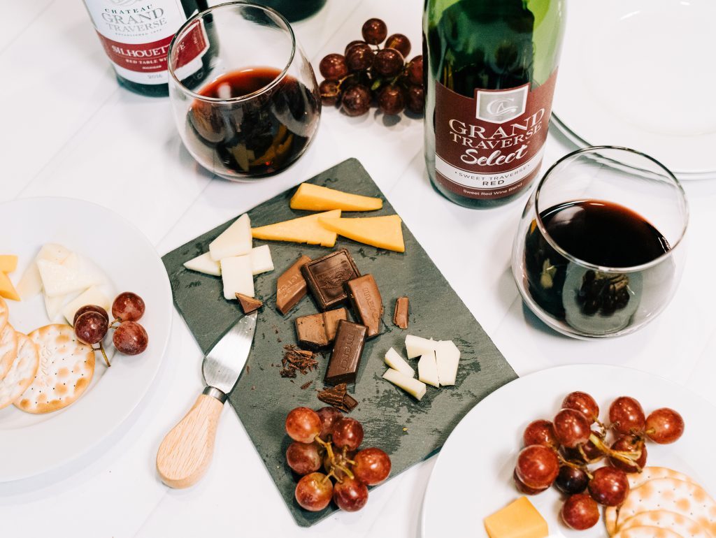 Charcuterie board with cheese, chocolate, grapes, and Chateau Grand Traverse wine