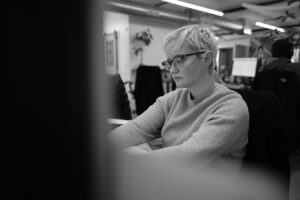 a woman with short hair and glasses works on her computer in an office