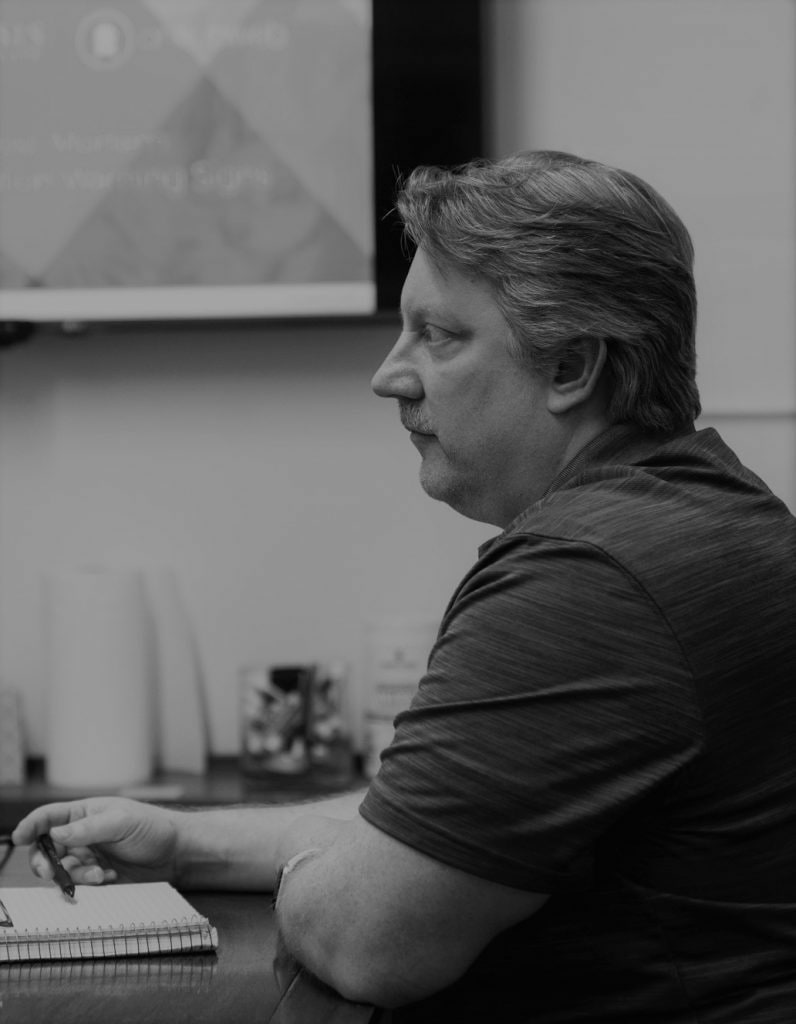 Man sits at a table with a notebook and pen, appears to think deeply