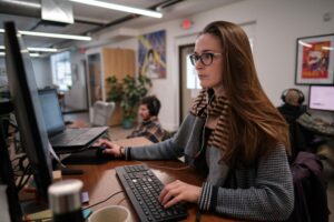 A female page experience expert works at a computer while wearing glasses and a scarf