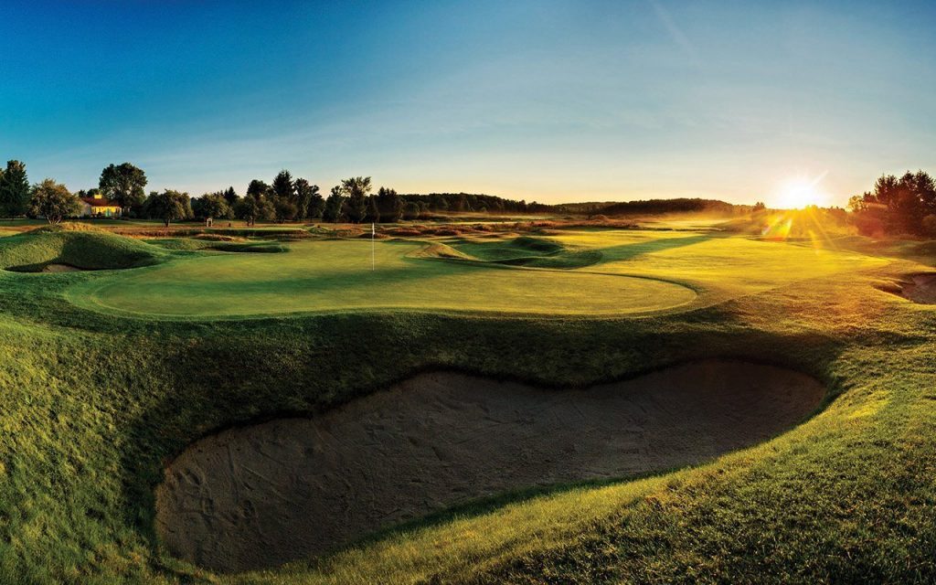 a golf course with sand and rolling hills as the sun peeks over the horizon in the evening on a clear day